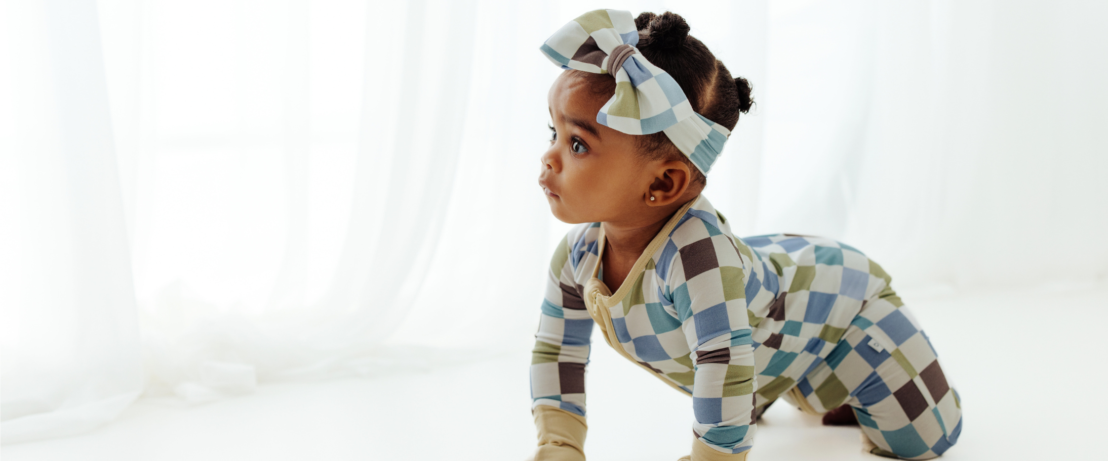 Baby wearing affordable luxury baby clothes. Luxe Checker bamboo sleeper and baby bow.
