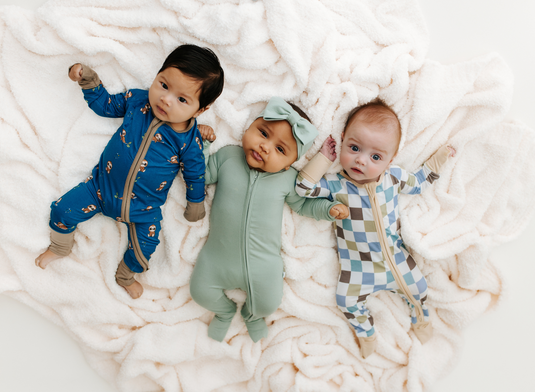 Three adorable babies laying next to each other in affordable luxury baby clothes.