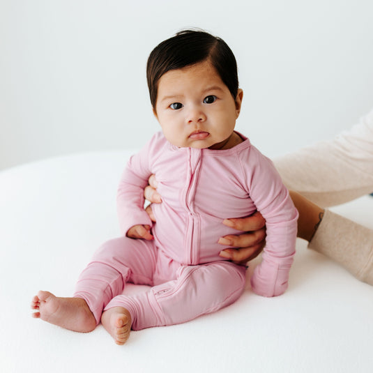 Baby in Petal Glow bamboo baby pajamas, a buttery-soft baby onesie in a delicate blush pink. A top pick in bamboo baby clothes and for heartfelt baby shower gifts.