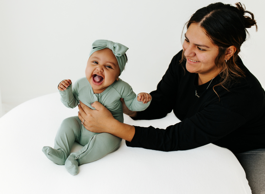 Mom and daughter laughing while baby is in an adorable baby girl's outfit.