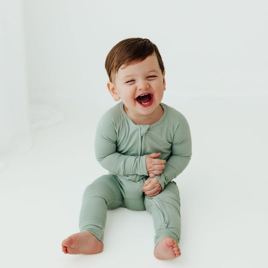 Child wearing a green onesie sitting on a white background