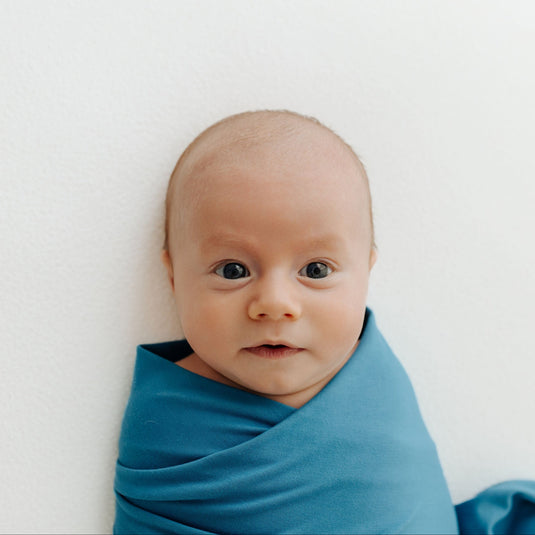 Baby snuggled in one of our Blue Charcoal Stretchy Swaddle Blanket, enjoying its ultra-soft bamboo fabric. A cozy and hypoallergenic must-have in bamboo baby clothes and perfect for Baby Shower Gifts.