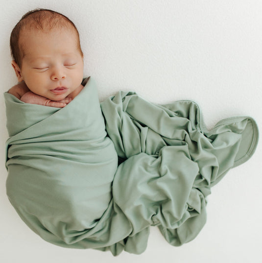 Baby sleeping in one of our Frosted Sage Stretchy Swaddle Blankets, wrapped in luxurious bamboo fabric for maximum comfort. A premium addition to bamboo baby clothes and great for Baby Shower Gifts.