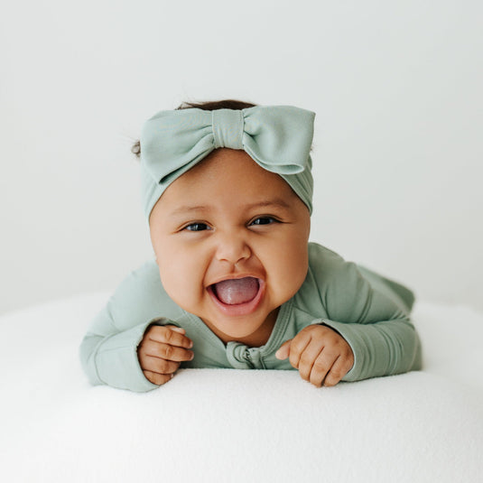 Baby laughing in Frosted Sage bamboo bow headband – a premium addition to bamboo baby clothes and adorable outfits.