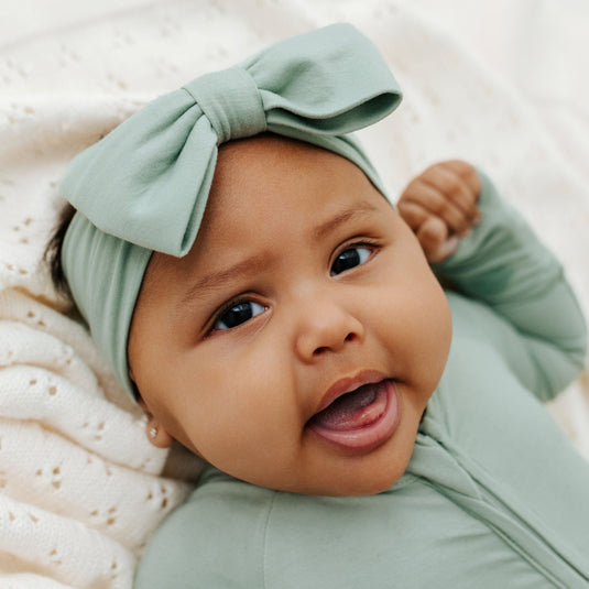 Baby wearing Frosted Sage bamboo bow headband – a cozy newborn essential. A top pick to pair with bamboo baby clothes and a must-have for baby shower gifts.