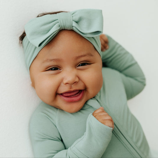 Baby laughing in Frosted Sage bamboo bow headband – a premium addition to bamboo baby clothes and a thoughtful baby shower gift.