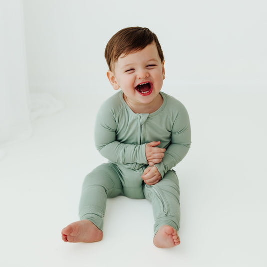 Baby laughing in Frosted Sage bamboo baby sleeper – a cozy, hypoallergenic sleeper perfect for delicate newborn skin. These baby sleepers are a must-have in bamboo baby clothes and a perfect baby shower gift.
