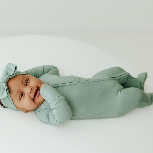Baby in Frosted Sage bamboo baby sleeper – a muted green, gender-neutral sleeper designed for all-day comfort. These baby sleepers are a favorite in bamboo baby clothes and a thoughtful baby shower gift.