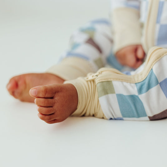 Baby feet in Luxe Checker bamboo baby sleeper – a buttery-soft, stretchy sleeper made for cozy naps. These baby sleepers are a go-to in bamboo baby clothes and a luxurious baby shower gift.