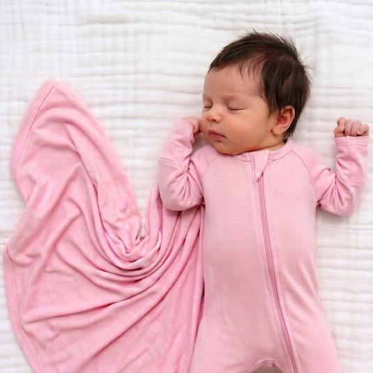 Newborn baby in a pink onesie lying on a textured white surface