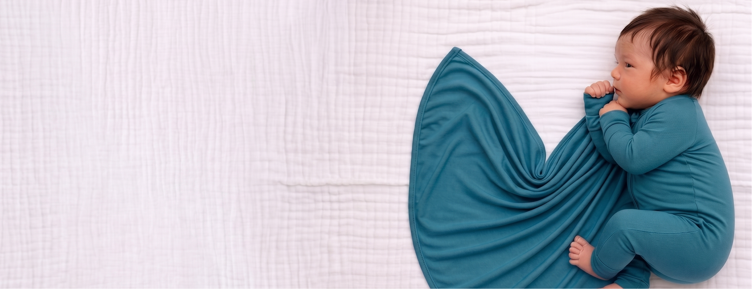 Baby in blue teal outfit lying on a white textured surface