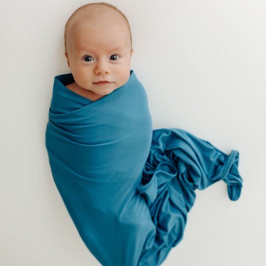 Baby wrapped in one of our Blue Charcoal Stretchy Swaddle Blankets, enjoying its ultra-soft bamboo fabric. A cozy must-have in bamboo baby clothes and perfect for Baby Shower Gifts.