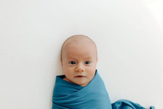 Baby snuggled in one of our Blue Charcoal Stretchy Swaddle Blanket, enjoying its ultra-soft bamboo fabric. A cozy and hypoallergenic must-have in bamboo baby clothes and perfect for Baby Shower Gifts.