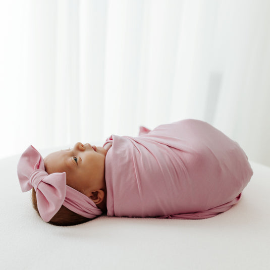 Baby wrapped in one of our Petal Glow Stretchy Swaddle Blankets. This ultra-soft newborn essential is a favorite in bamboo baby clothes and an ideal pick for Baby Shower Gifts.