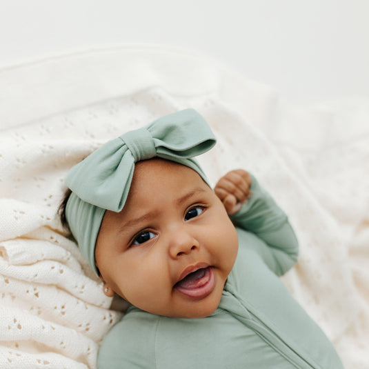 Baby wearing our Frosted Sage bamboo baby bows, a cozy newborn essential. A top pick to go with bamboo baby clothes and a must-have for baby shower gifts.