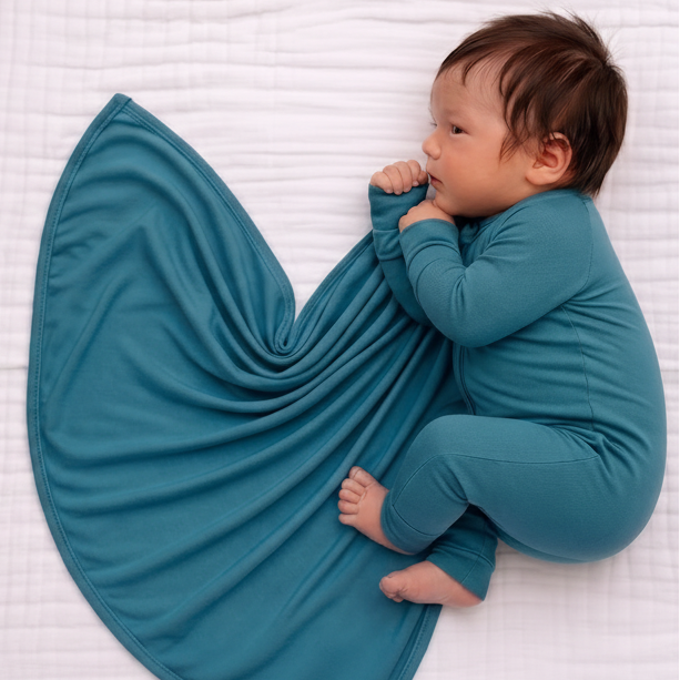 Baby in teal outfit lying on a white textured surface