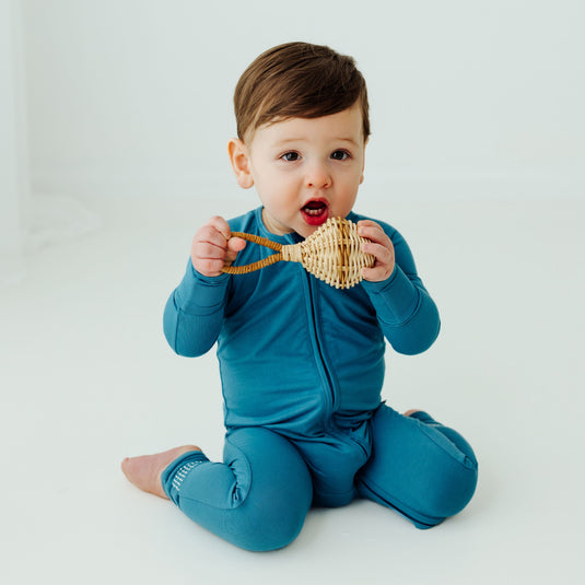 Baby in blue outfit holding a wooden toy against a white background