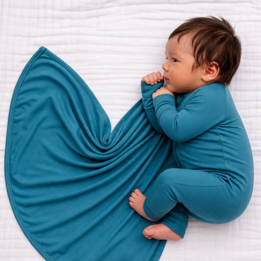 Blue Charcoal | Newborn baby in a blue bamboo sleeper laying on side with a stretchy swaddle blanket next to them in a newborn set.