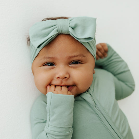 Baby wearing a green outfit and headband with a white background
