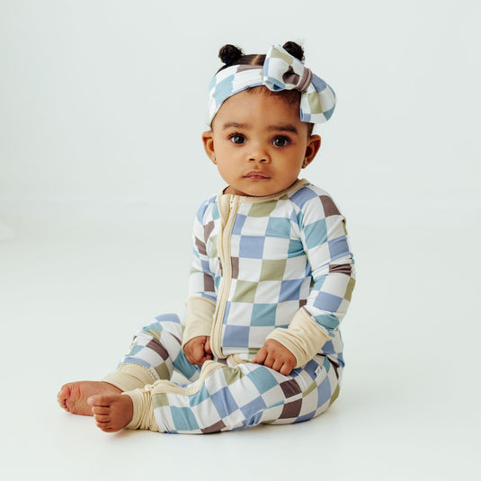 Baby wearing a checkered outfit and headband with animal ears on a white background